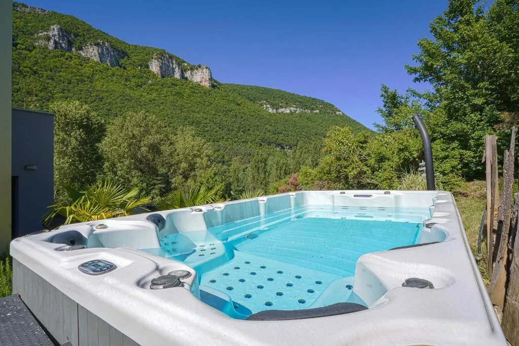 Grand spa extérieur rempli d'eau claire face à une vallée boisée et des falaises calcaires